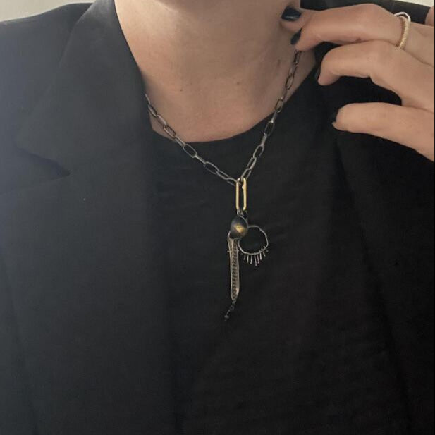 Person wearing a black shirt with a unique necklace featuring a pendant.
