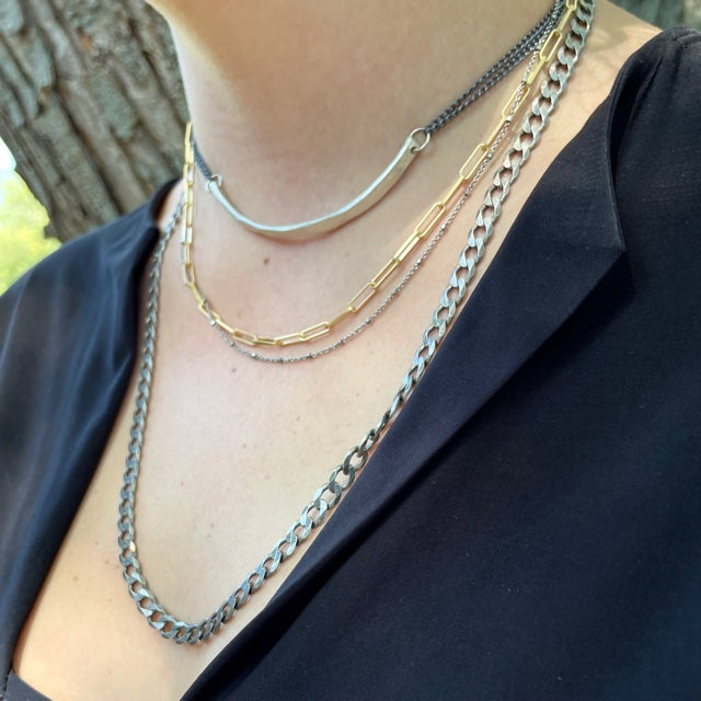 Person wearing multiple chain necklaces with a blurred natural background