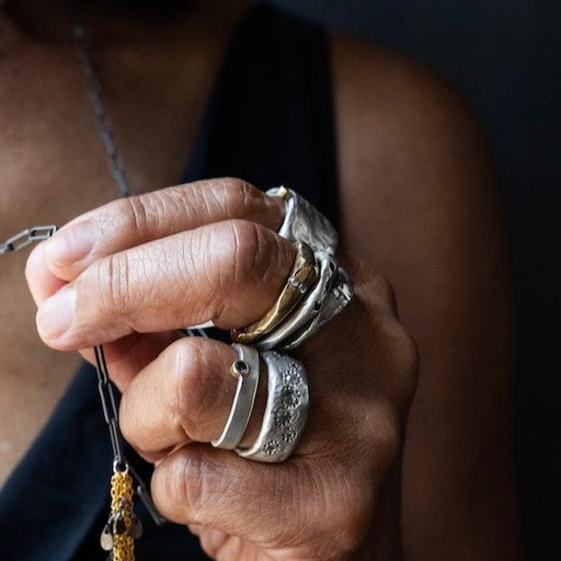 Close-up of a hand wearing multiple silver rings with a blurred background