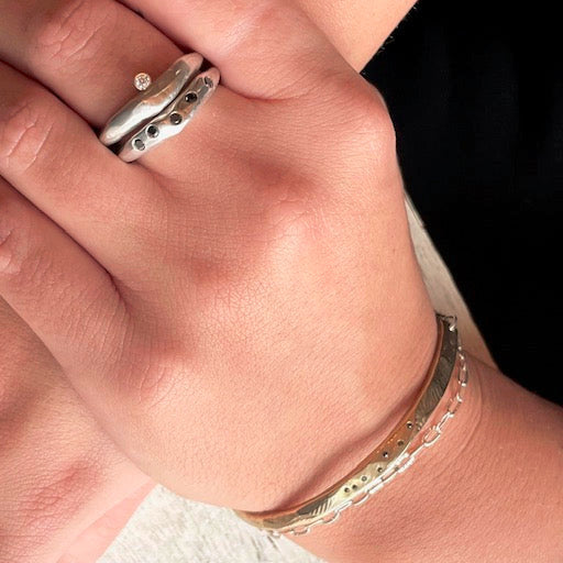 Skipping Stones Simple Bracelet in Bronze with Black Diamonds and the Odyssey Ring in Silver and Constellation Ring in Silver on a person