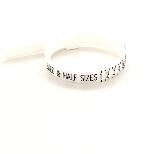 A ring sizer tool with markings for measuring ring sizes, placed on a plain background.