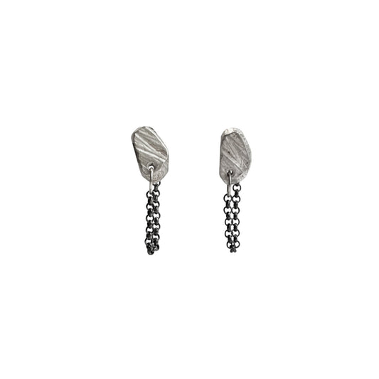 The Stone Stud with Chain Earrings feature a classic stud design, elevated by a delicate chain that drapes gracefully from the lobe. The attached chain adds movement and intrigue, creating a dynamic look that's both sophisticated and playful. Their versatile design allows for various wearing styles - traditionally in the lobe, or creatively styled up the ear for a more dramatic effect.