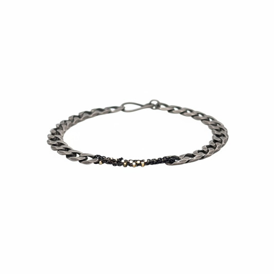 The Binding Light Bracelet pairs a hand-finished oxidized curb chain with a woven center chain of black with gold highlights, symbolizing the way contrast becomes resilience. It evokes the beauty of what’s been mended, tended, or held with intention.&nbsp;