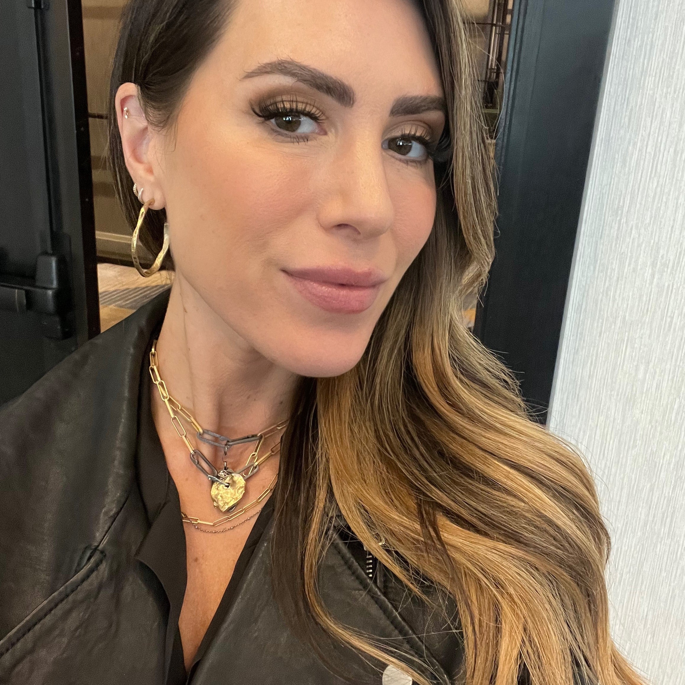 Woman with layered necklaces featuring the Gold Link Chain and Stonehenge hoop earrings indoors