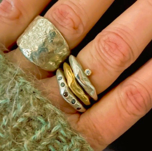 Close up of Origin Ring in Silver and other Stacked Silver and Bronze Rings shown on persons hand 